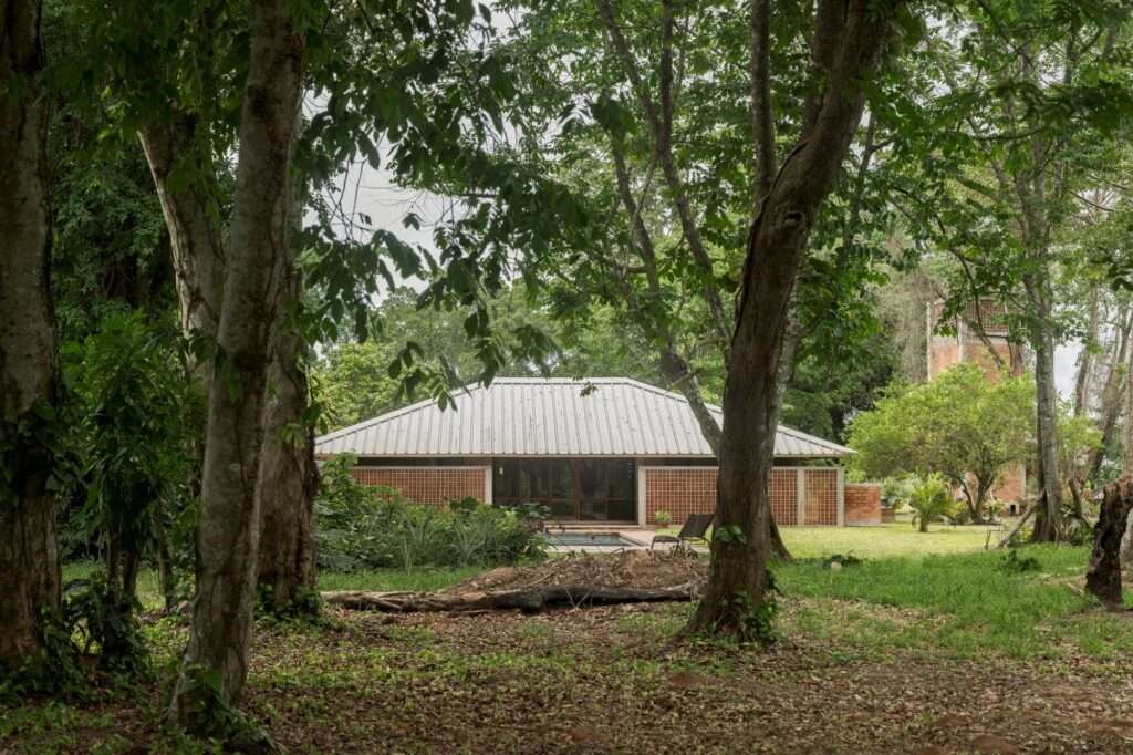 Symmetrical modern villa with an aluzinc roof and red brick brickwork nestled among dense Amazon rainforest trees.