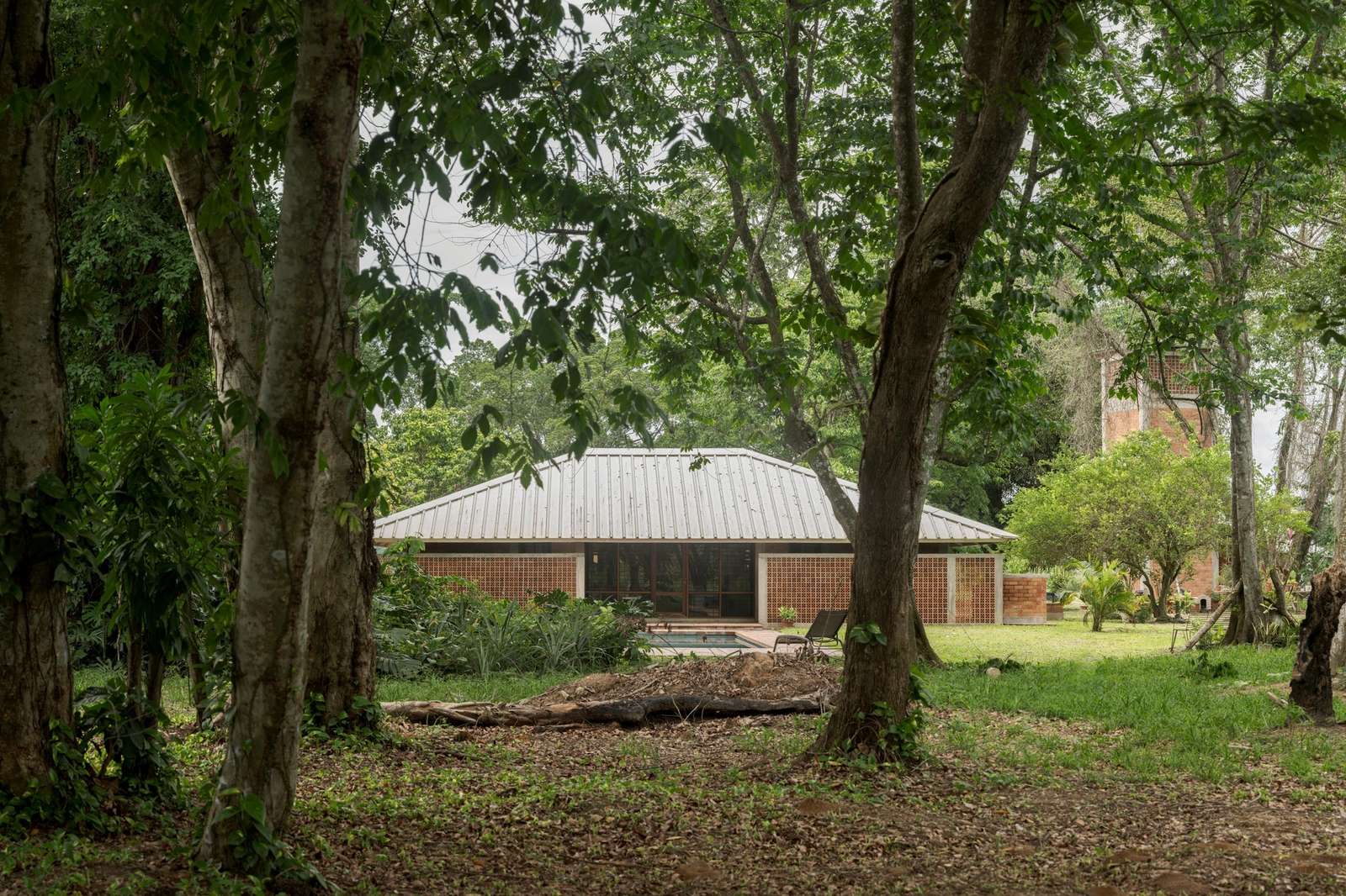 Symmetrical modern villa with an aluzinc roof and red brick brickwork nestled among dense Amazon rainforest trees.