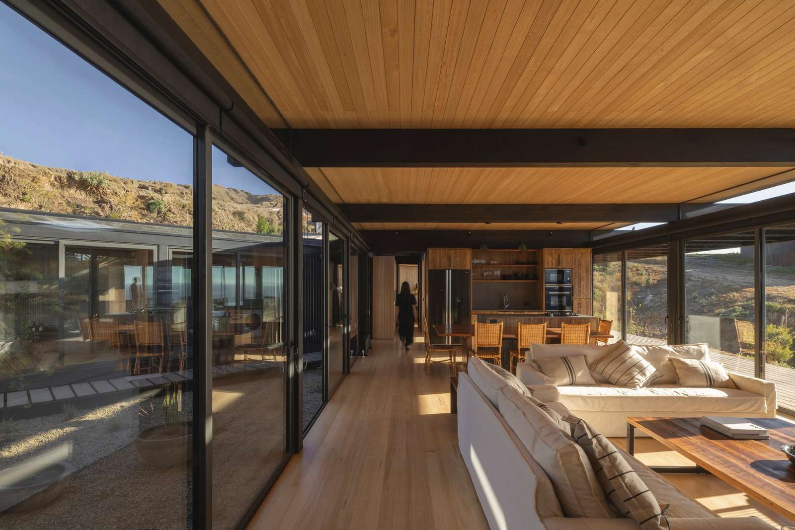 Interior living room of Matanzas Beach House featuring wooden ceilings and expansive glass walls overlooking the ocean.