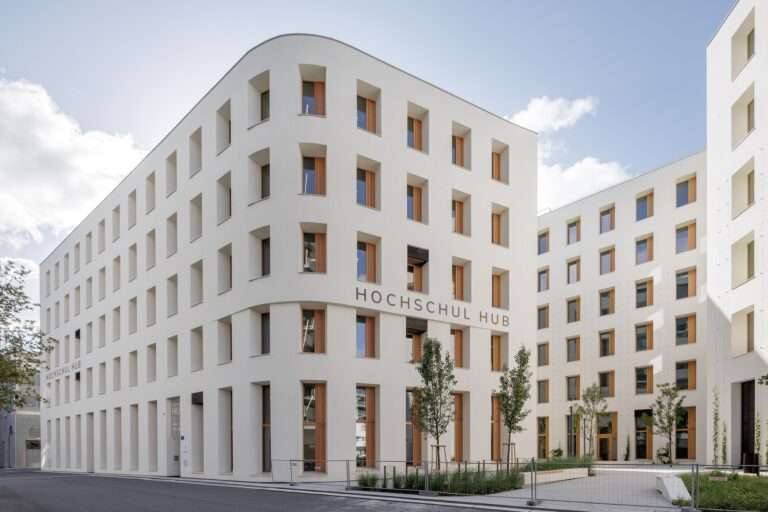 Exterior corner view of ROBIN Seestadt Aspern building with white load-bearing walls and deeply recessed wooden windows.