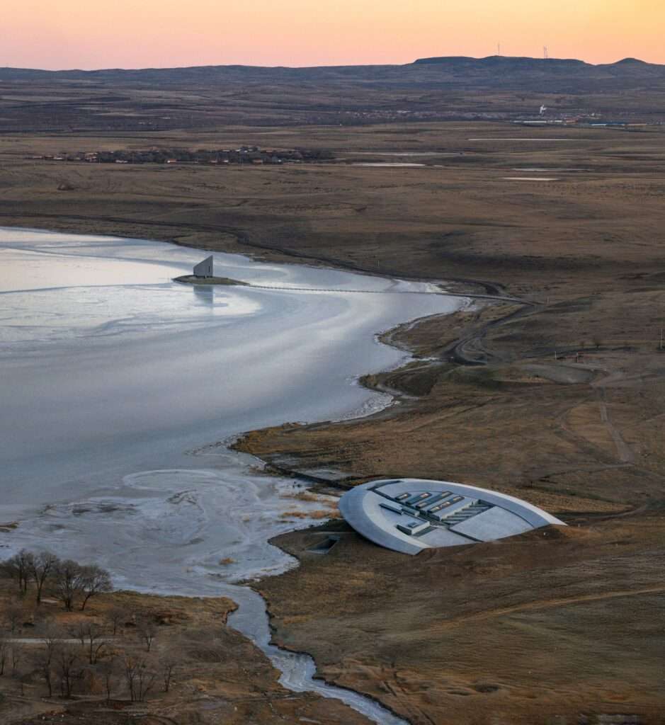 Panoramic view of the site featuring both the underground Prairie Ark and the vertical Nomad's Beacon tower by the lake.