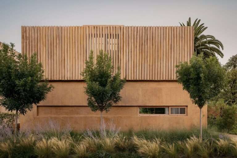 Exterior facade of JR House showing the textured concrete walls and vertical wooden slats blending with surrounding lush greenery.
