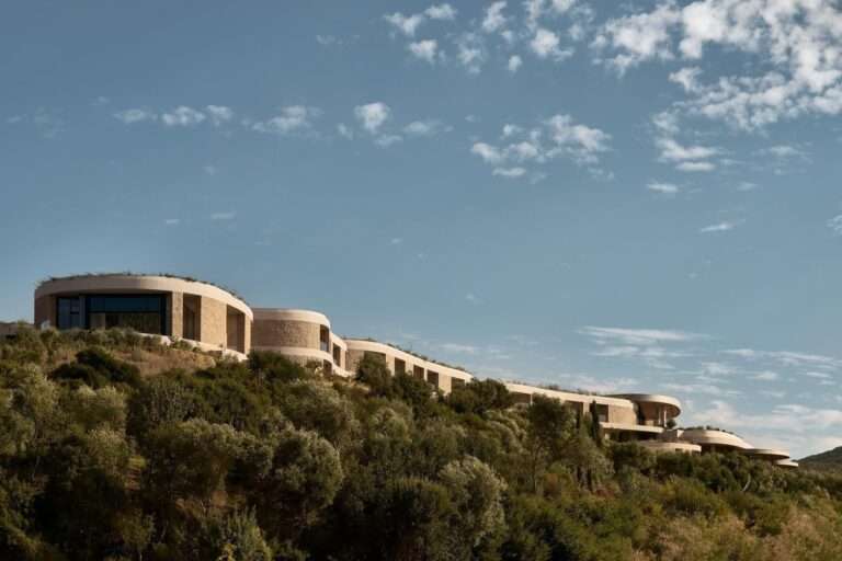 Close-up of terraced concrete and stone earth-sheltered resort suites integrated into a Mediterranean hillside forest.