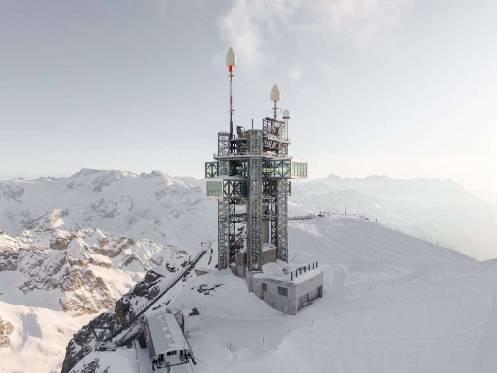 Aerial view of the Titlis mountain station and tower covered in snow with cross-shaped cantilevering glass volumes in Switzerland.