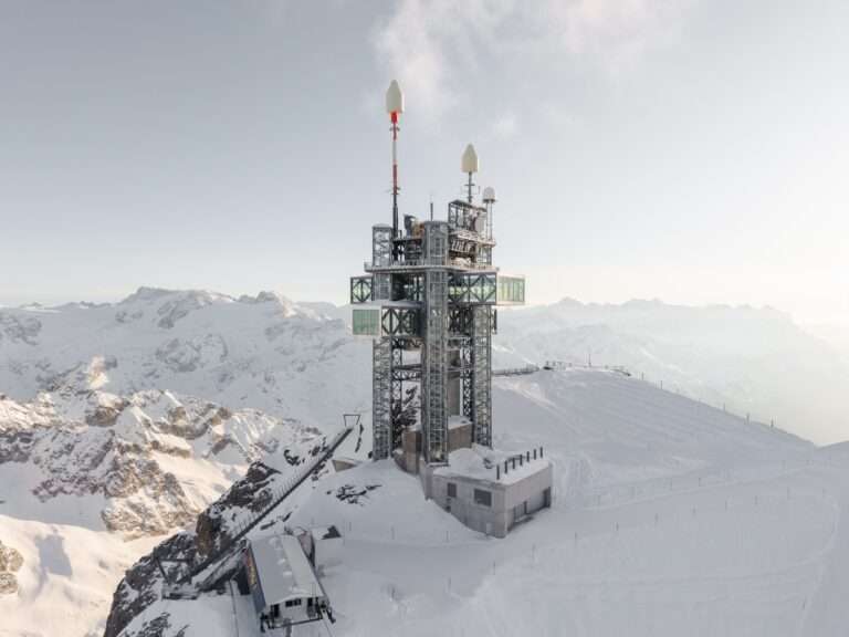 Aerial view of the Titlis mountain station and tower covered in snow with cross-shaped cantilevering glass volumes in Switzerland.