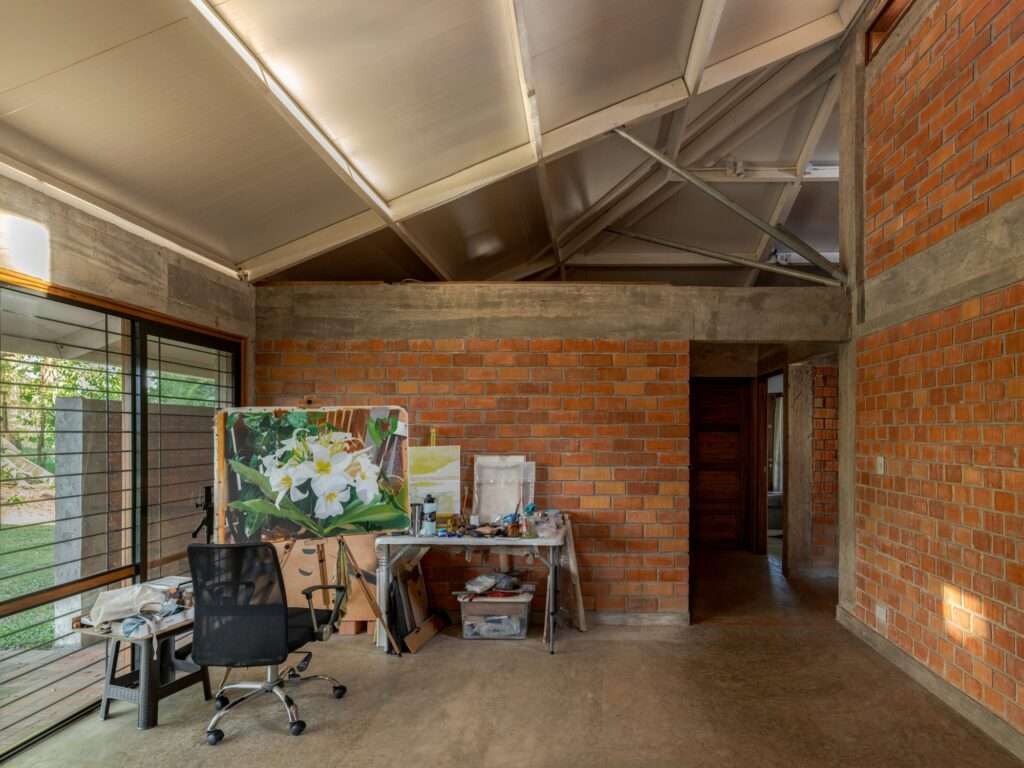 Interior art studio room inside Villa E featuring exposed red clay brick walls, polished concrete floor, and an artist easel with a floral painting.