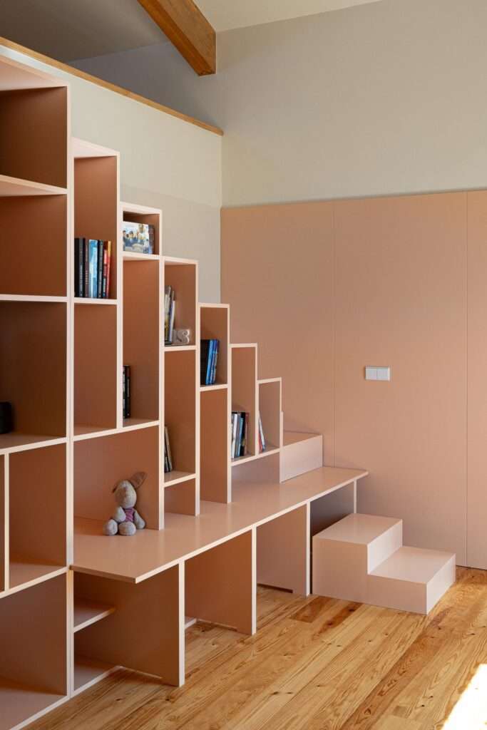 Close-up of a custom-designed millennial pink wooden staircase integrated with geometric open bookshelves and storage compartments on a light wood floor.