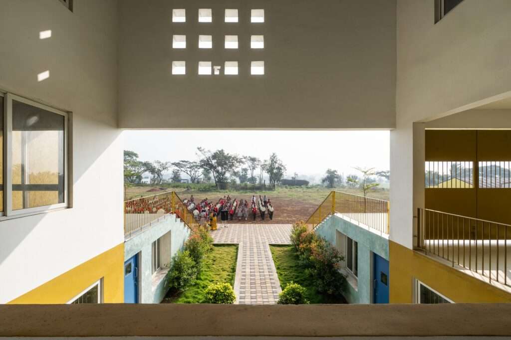 Architectural framed view from an upper-level corridor overlooking a landscaped courtyard pathway where students gather in an open field.