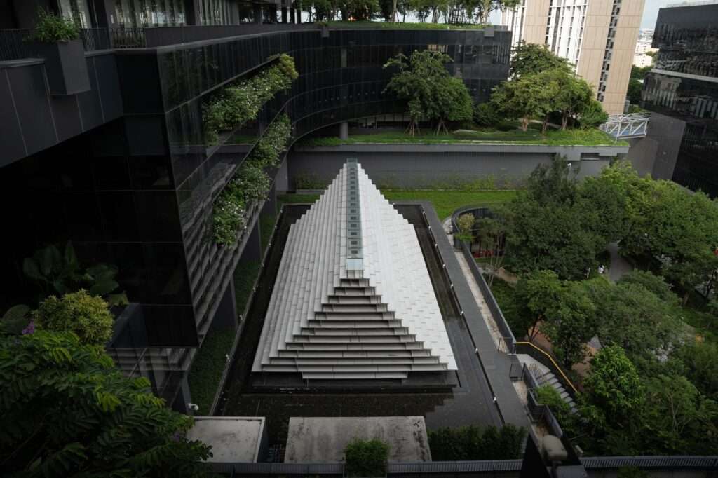 Aerial perspective of the stepped, glass-clad meditation pavilion situated on a reflective water surface in a courtyard.