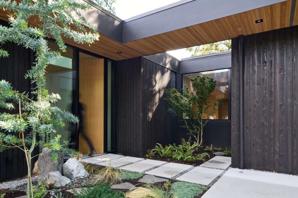 Modern residential entrance with a covered wooden ceiling and a small garden courtyard at Layer House.