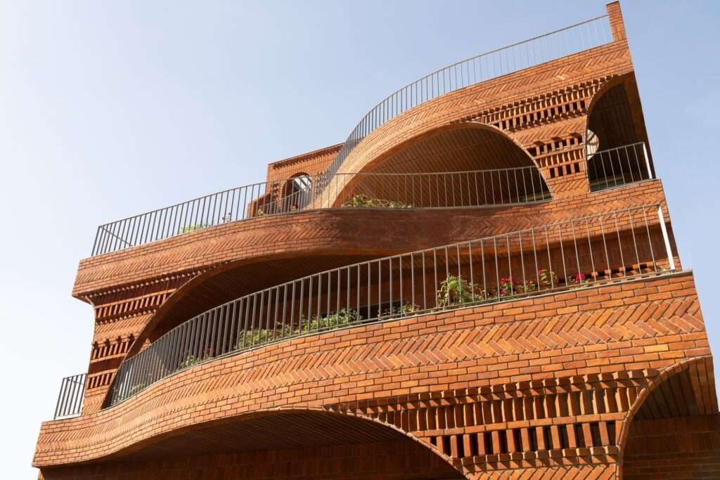 A minimalist concrete staircase with a steel balustrade featuring two circular brick-framed windows where young children are sitting.