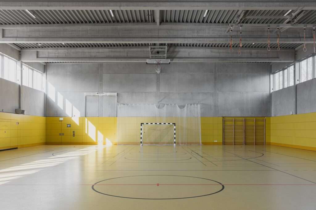 Indoor sports hall of the SK Berlin school with yellow wall paneling and concrete ceiling.