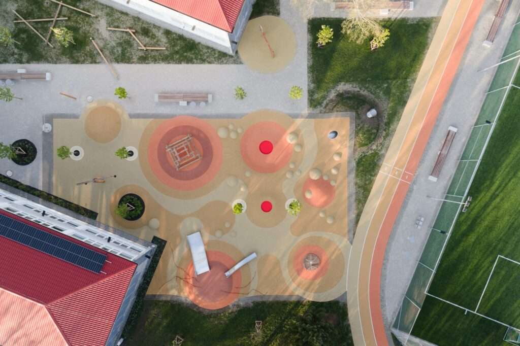 Aerial view of a school sports complex featuring a running track, soccer field, and a colorful, modern playground with various play equipment.