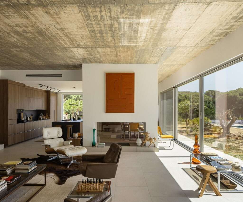 Minimalist staircase leading down to a hallway featuring an orange patterned rug, a modern leather swivel armchair, an antique wooden panel on the wall, and a stone griffin statue.