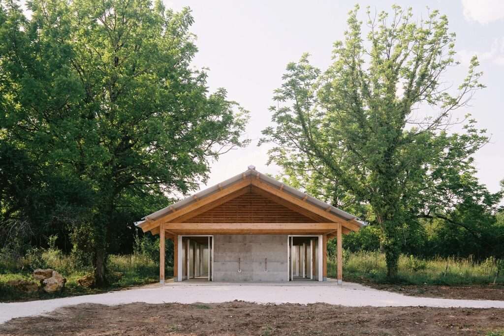 Symmetric front elevation view of the Gardeners' Shelter featuring a timber gable roof frame and central concrete volume flanked by translucent doors.