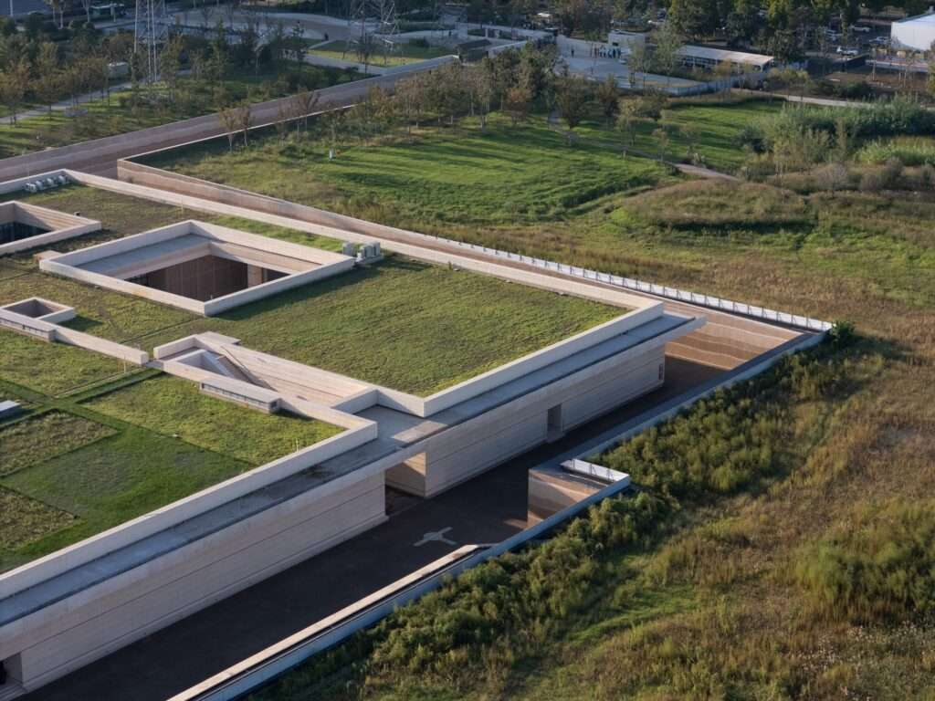 Elevated close-up of a subterranean museum wing showcasing sunken courtyards, concrete pathways, and lawns merging into natural wetlands.