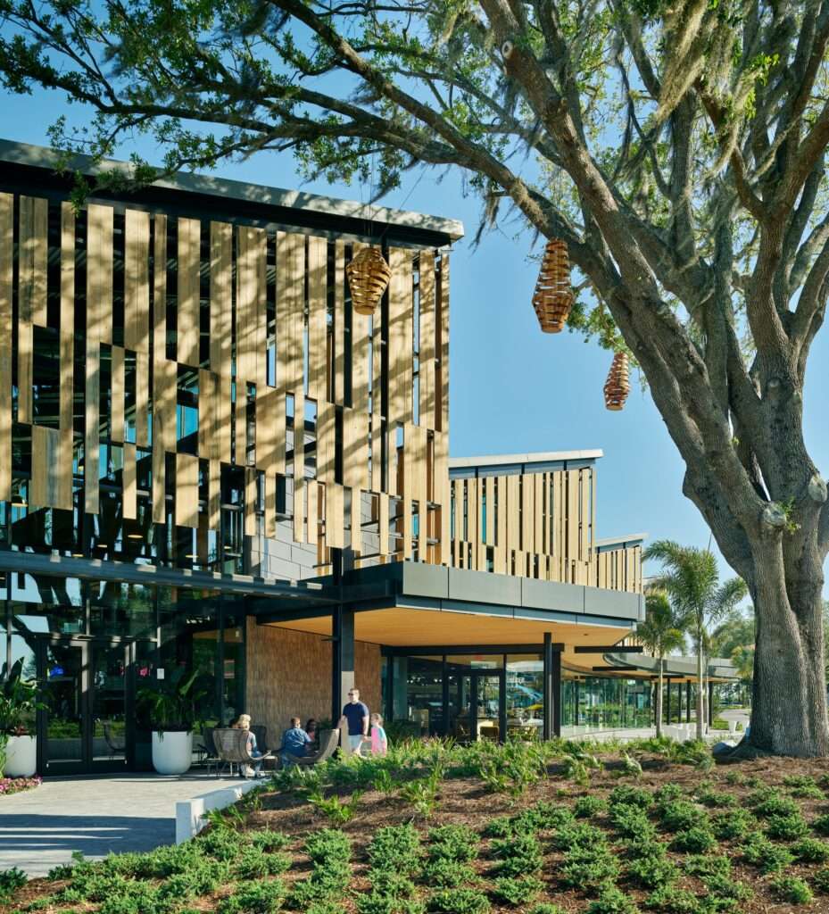 Exterior view of The Landing building facade showing vertical wooden screen panel filters and integrated mature trees under a clear blue sky.