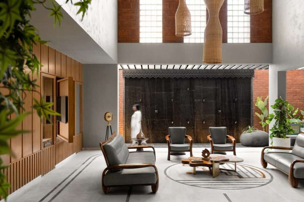 A modern double-height interior living room with gray seating, wooden wall paneling, hanging wicker light fixtures, and a large indoor water feature wall.