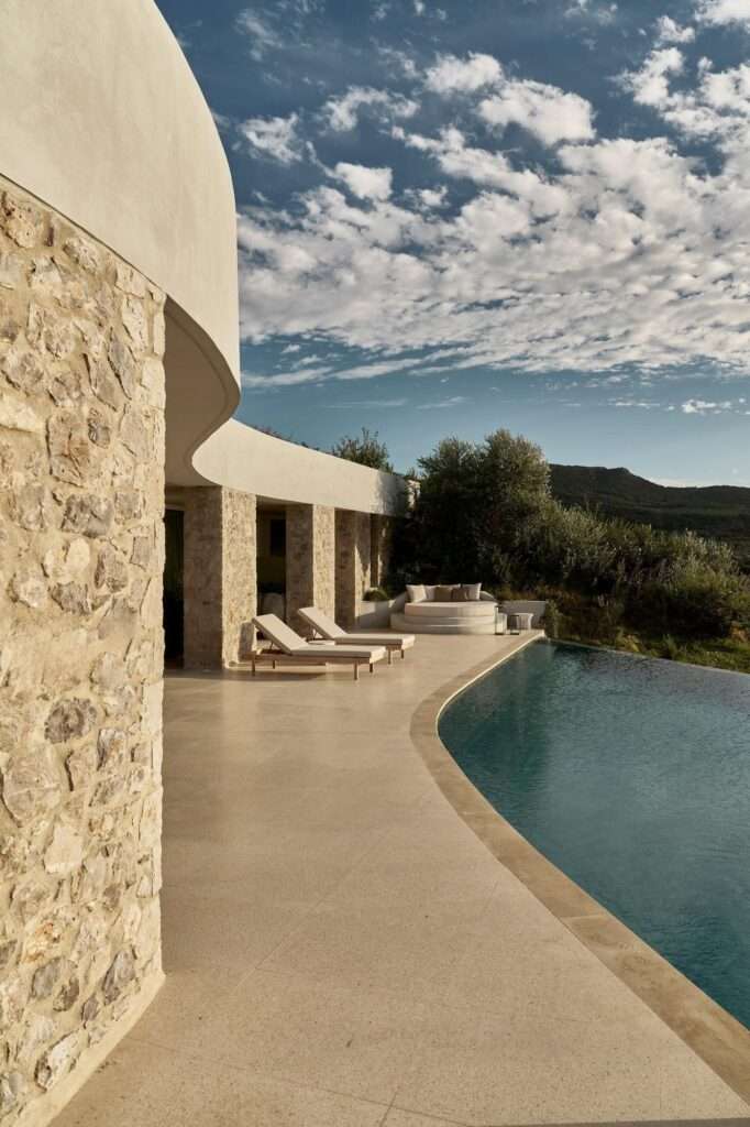 Top-down aerial drone view of a leaf-shaped infinity pool and sun deck integrated into dense Mediterranean vegetation.