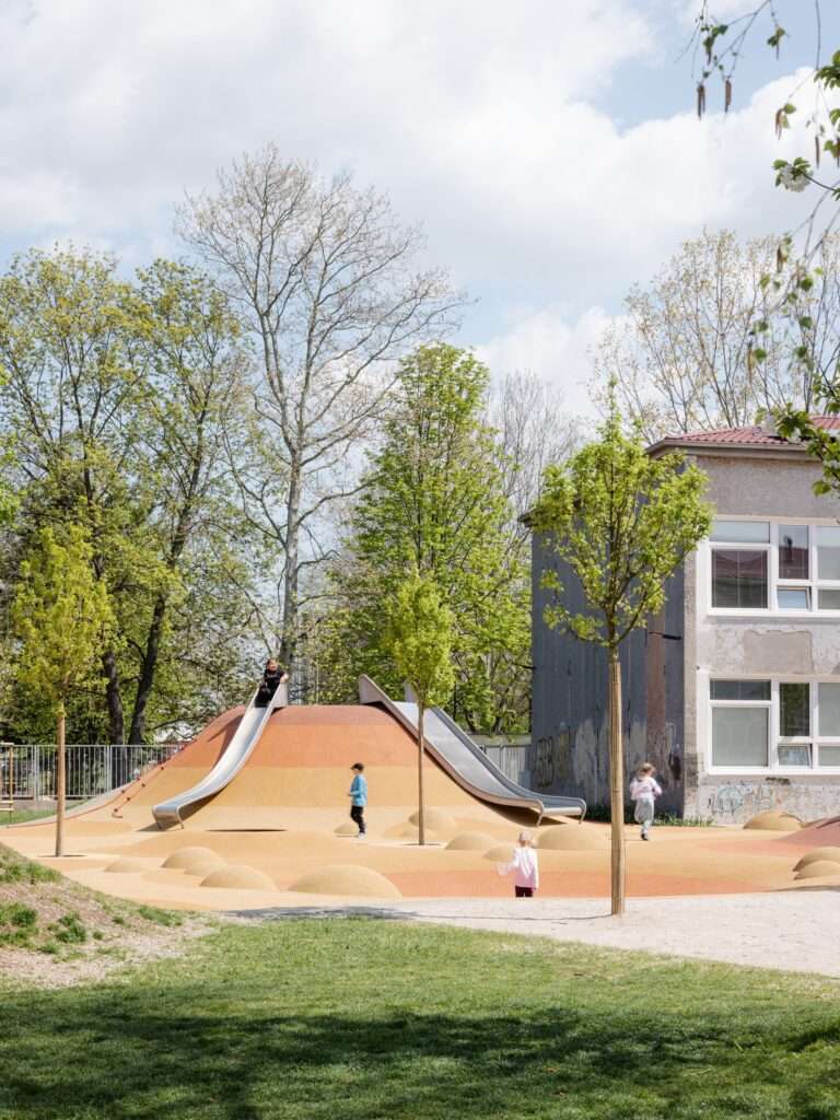 Children playing on large, curved, colorful slides in a modern school playground in Trnava.