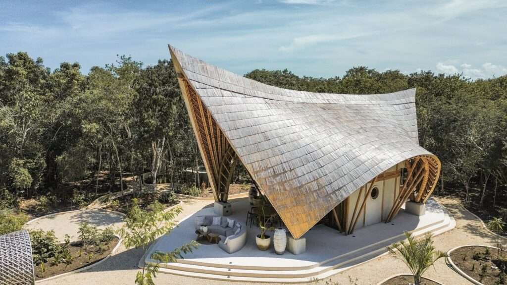 Aerial drone view of CORA Villa in Tulum, showcasing its massive curved sculptural bamboo roof blending into the surrounding Mayan jungle canopy.