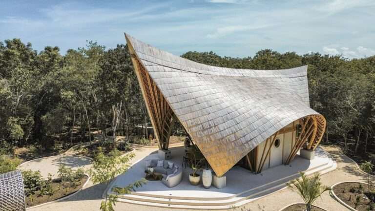 Aerial drone view of CORA Villa in Tulum, showcasing its massive curved sculptural bamboo roof blending into the surrounding Mayan jungle canopy.