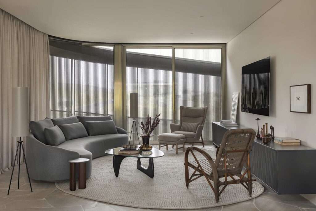 Modern interior living room of Casa Circular featuring a curved gray sofa, elegant round area rug, minimalist furniture, and a large sliding glass window looking out onto the metallic sunshades.