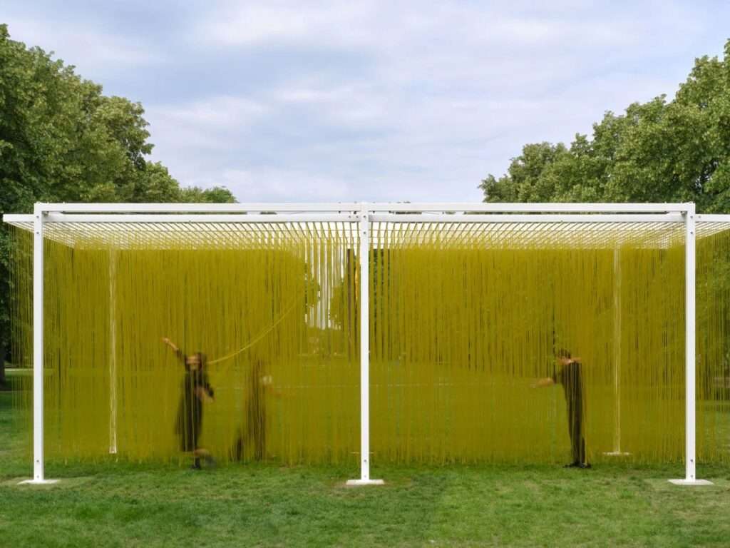 Wide shot of Penetrable BBL Jaune kinetic sculpture by Jesus Rafael Soto at Serpentine Galleries London, showing visitors walking through thousands of hanging yellow PVC tubes inside a white steel frame.
