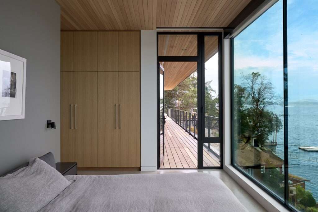 Modern bedroom with large sliding glass doors opening onto an exterior deck overlooking the sea.