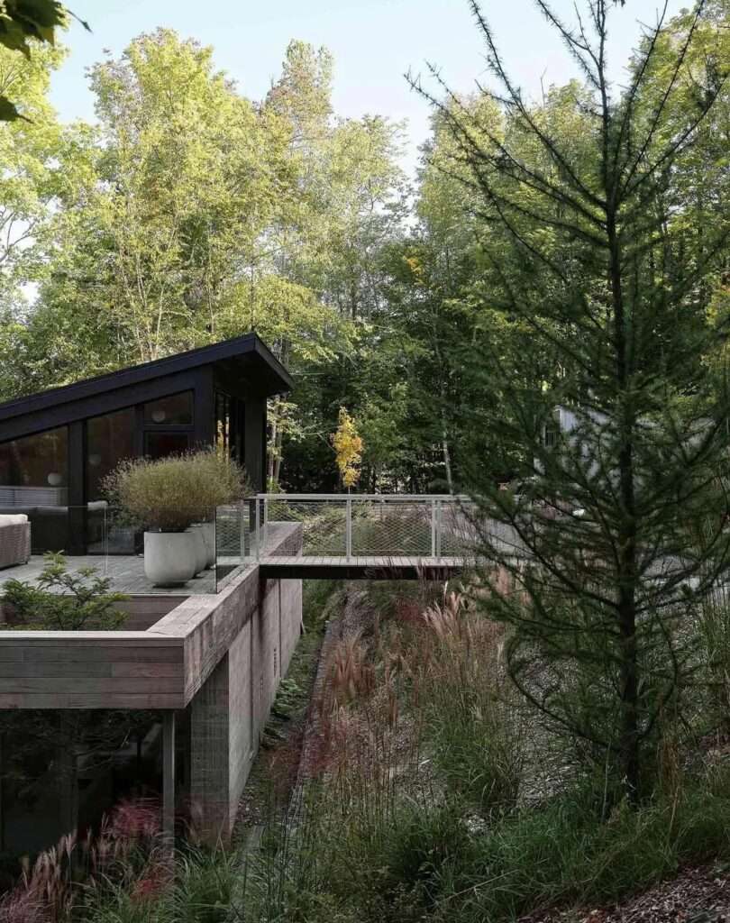 Aerial drone view of the Counter-Slope House nestled amidst a dense green forest canopy along the deep blue shoreline of Lake Memphremagog.