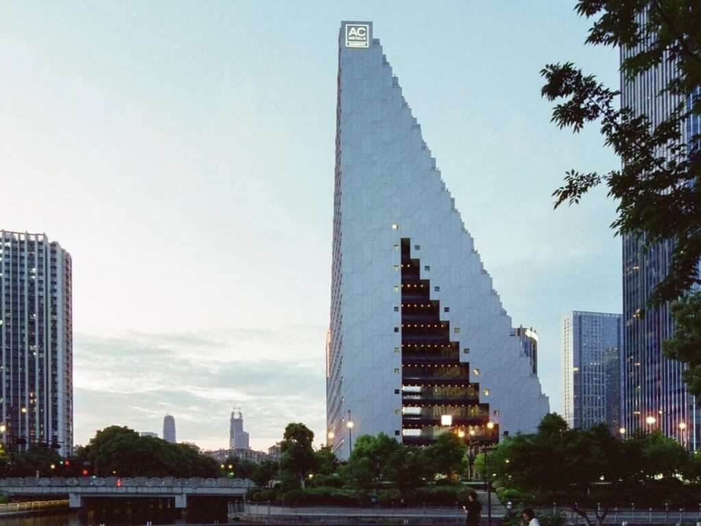 Exterior dusk view of Hangzhou Prism by OMA showing its large geometric cut-out void and sloped stepped pyramid form against a clear sky.