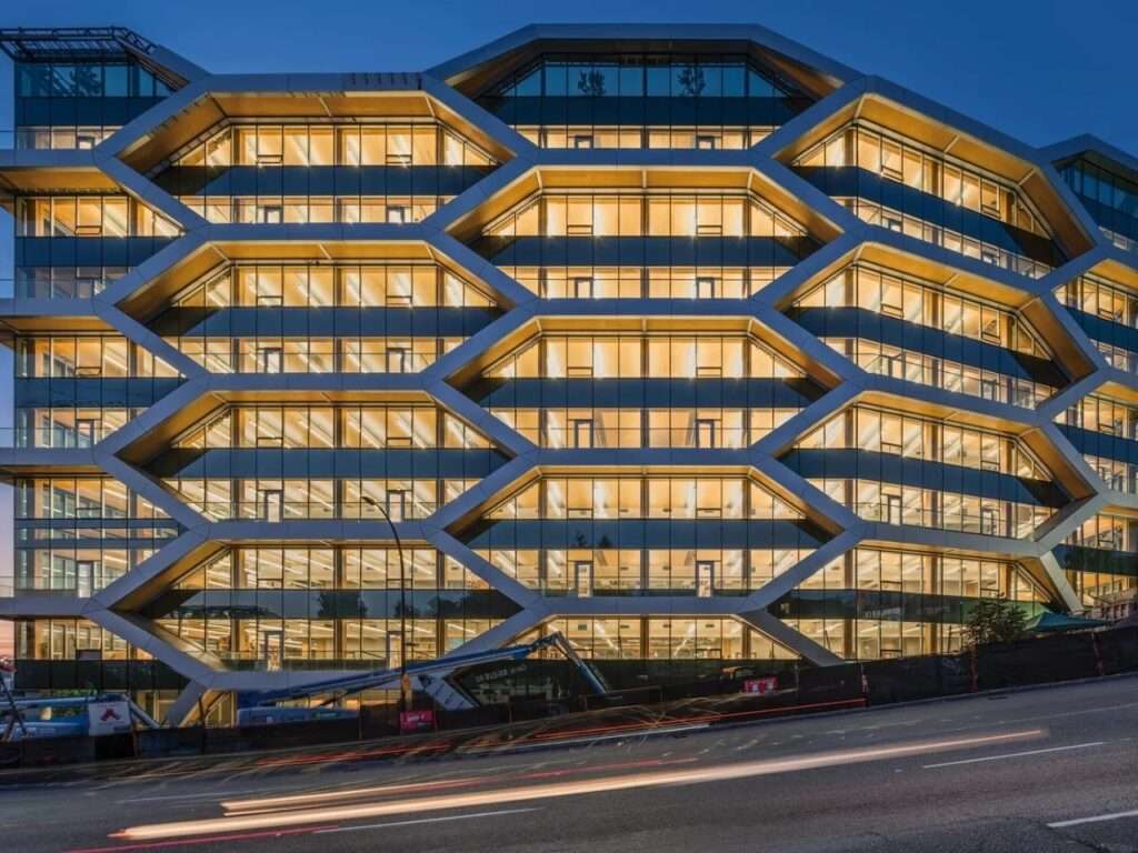 Illuminated honeycomb glulam timber facade of The Hive building in Vancouver at night, showcasing innovative seismic structural design.