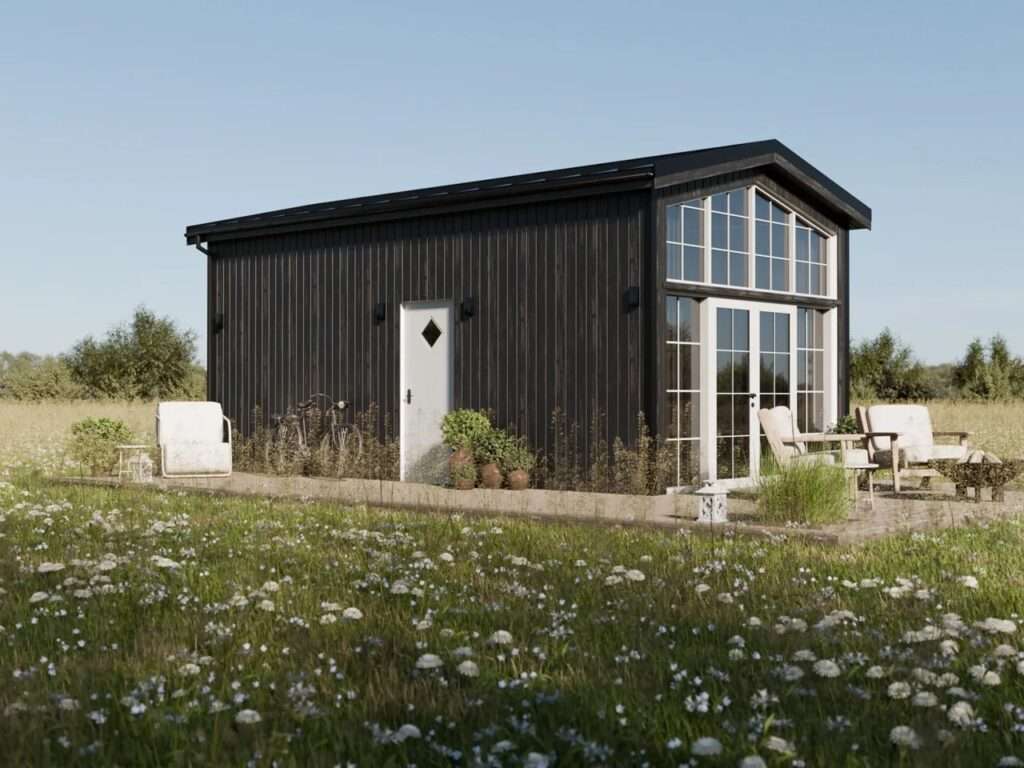 Exterior view of the Lucia tiny house featuring dark spruce timber cladding, a metal gable roof, and a large front glass facade facing a green meadow.
