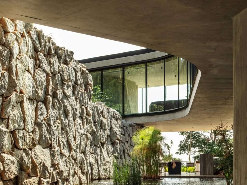 Xingu House curved concrete ceiling cantilevered over an ancient rough stone wall with a reflecting pool below.