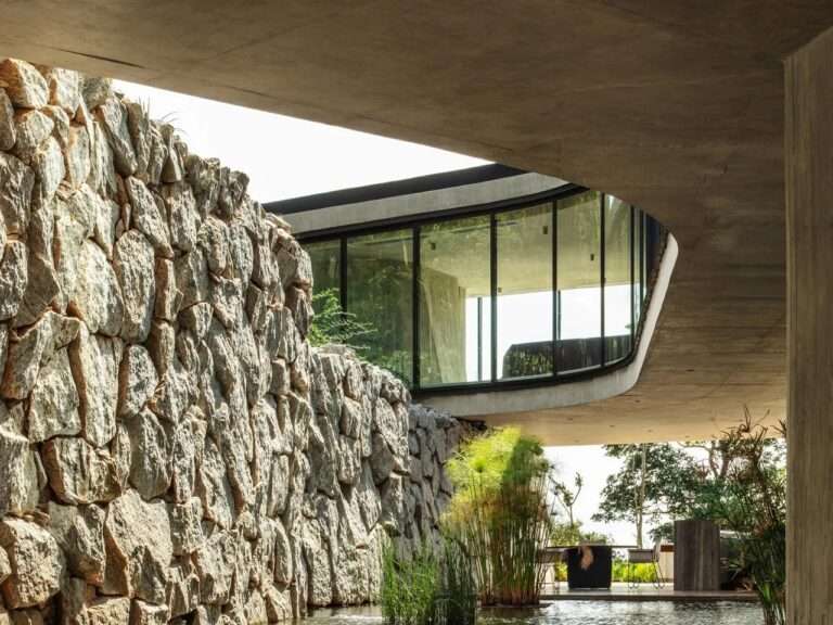 Xingu House curved concrete ceiling cantilevered over an ancient rough stone wall with a reflecting pool below.