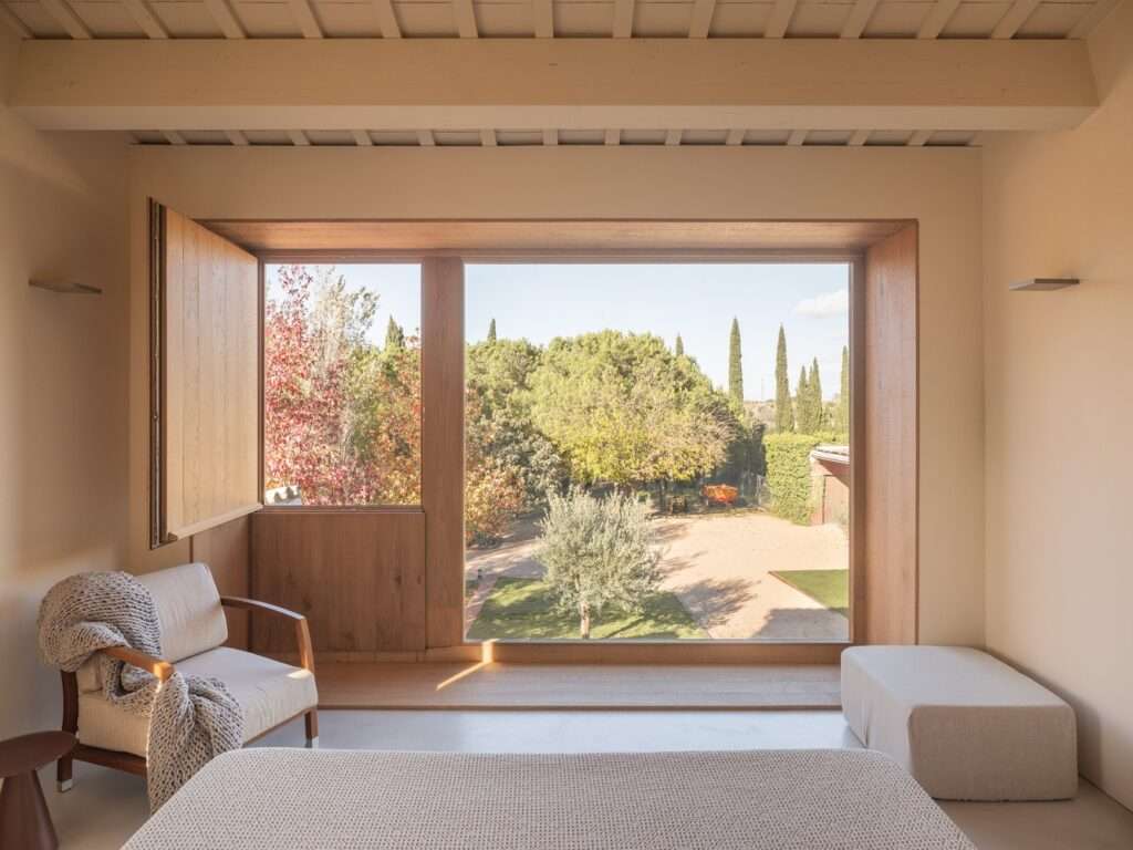 Minimalist bedroom interior with a large square panoramic window overlooking a green garden and courtyard in House 2302.