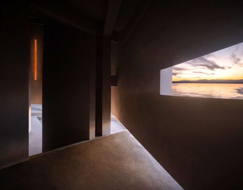 Interior view of the Prairie Ark looking out through a large window toward the sunset over the frozen lake.