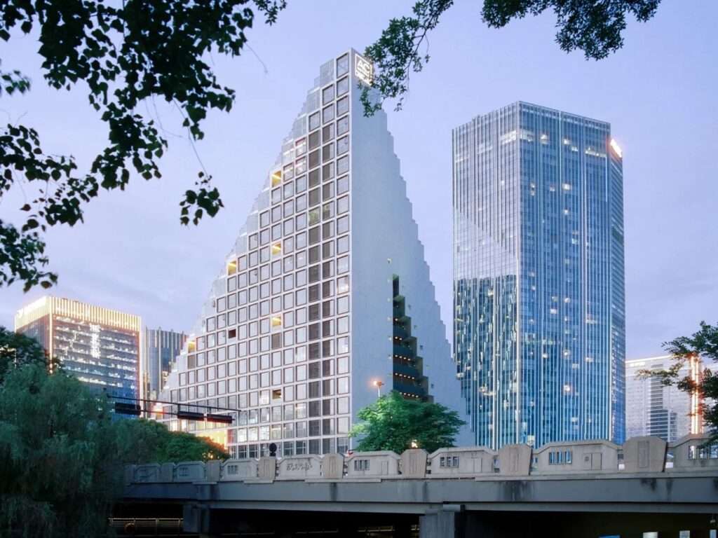 Hangzhou Prism high-rise building with a dramatic diagonal cut side facade standing next to modern glass skyscrapers at twilight.