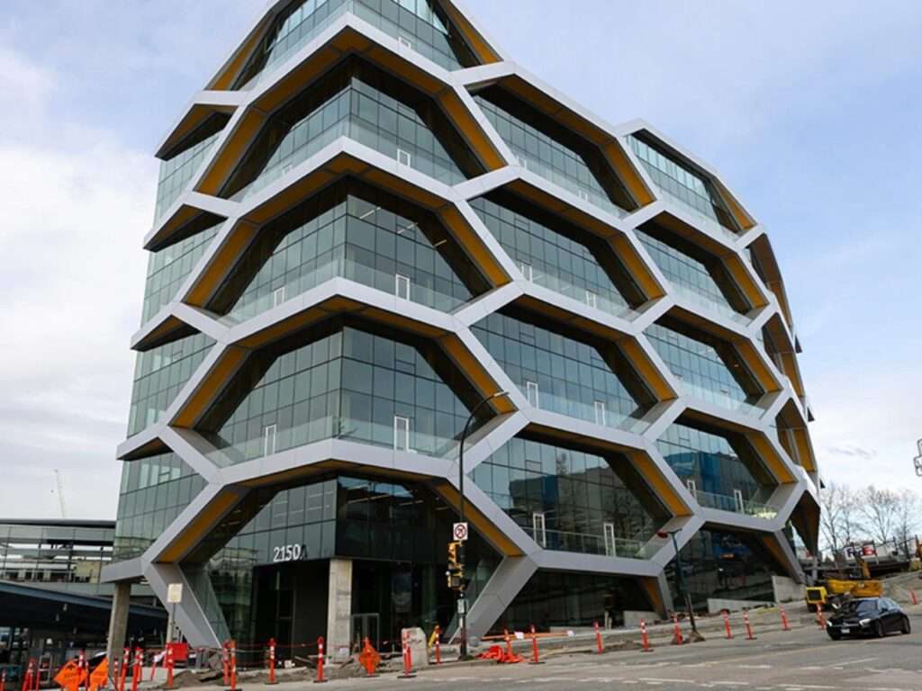 Street-level view of The Hive building in Vancouver featuring an exposed honeycomb glulam exoskeleton and large glass curtain walls.