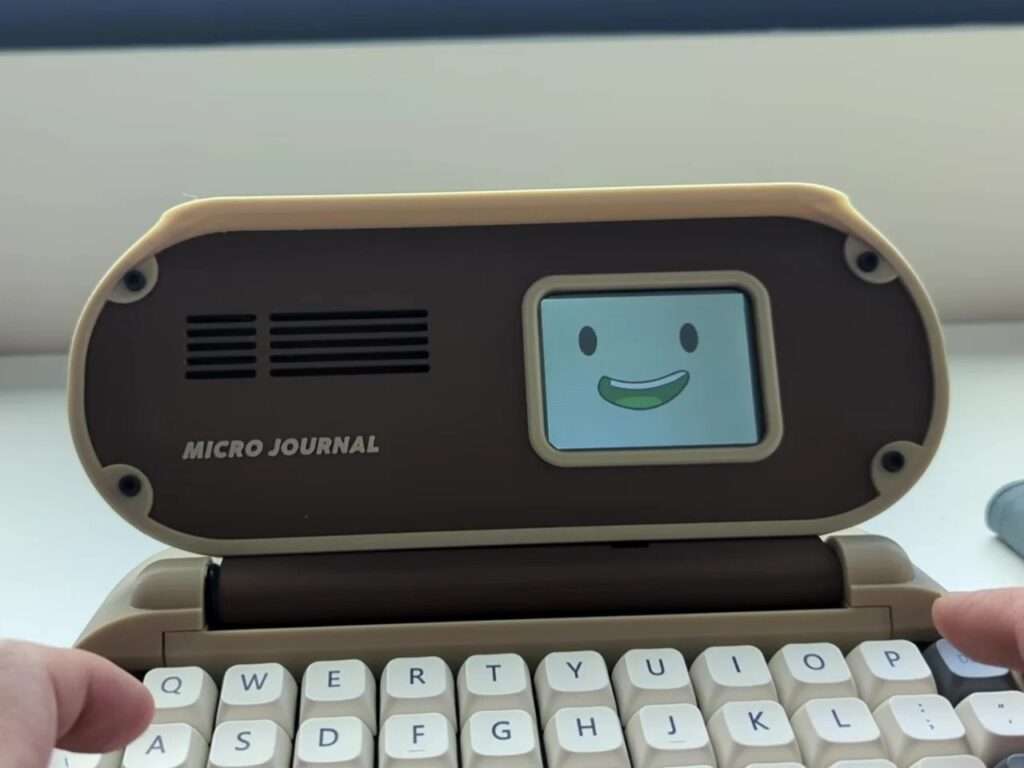 A side profile view of a person holding the closed Micro Journal Rev.6.1 device, showing its physical power switch, USB-C charging port, and hand-assembled structural texture.