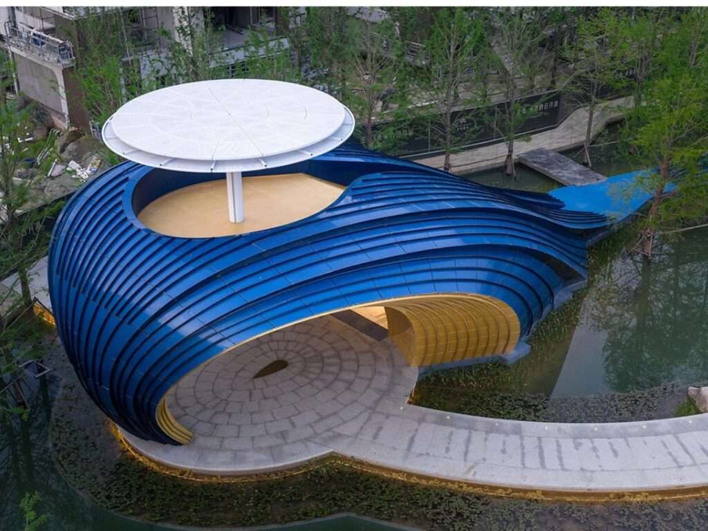 Close-up of the curved blue aluminum panels of the Whale Gate pavilion slanting upwards against a clear blue sky.