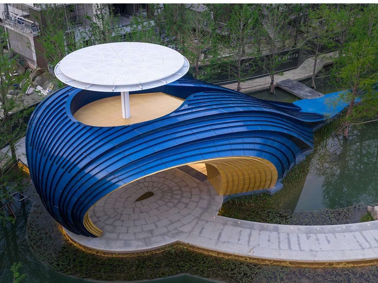 Close-up of the curved blue aluminum panels of the Whale Gate pavilion slanting upwards against a clear blue sky.