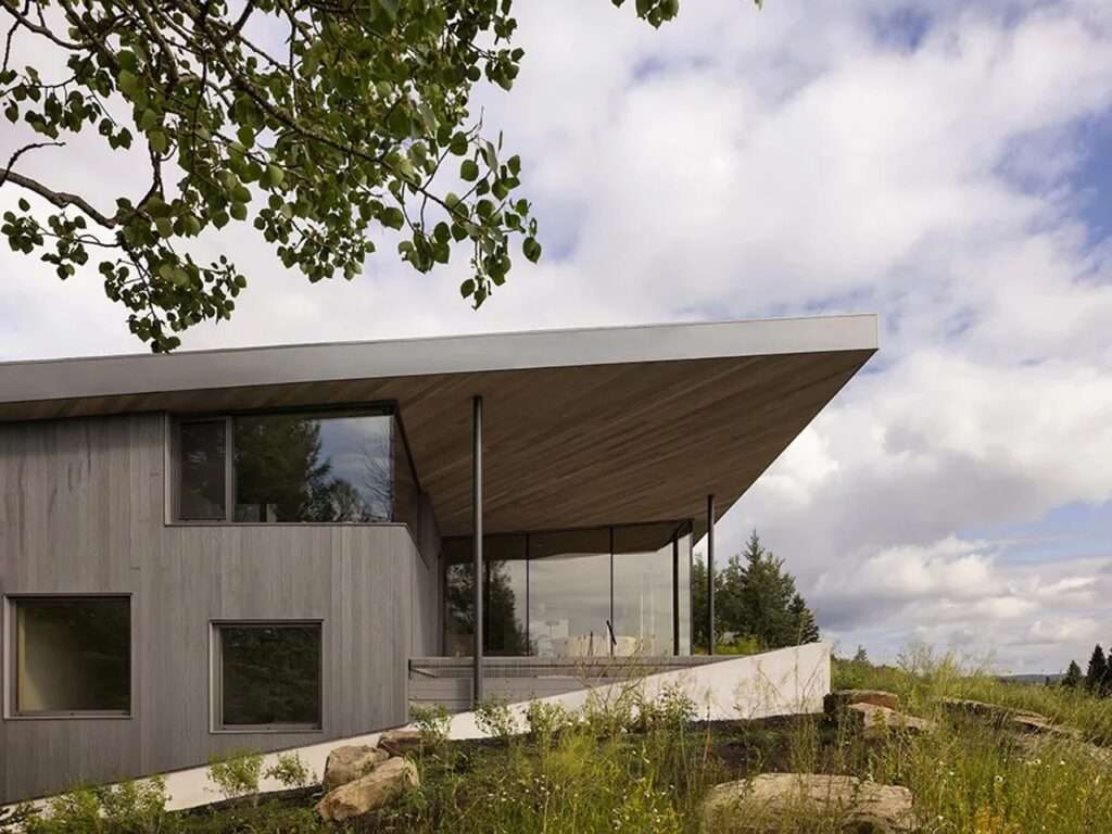 Dramatic angled roof overhang and large glass walls of Cut Out House overlooking a grassy hillside.
