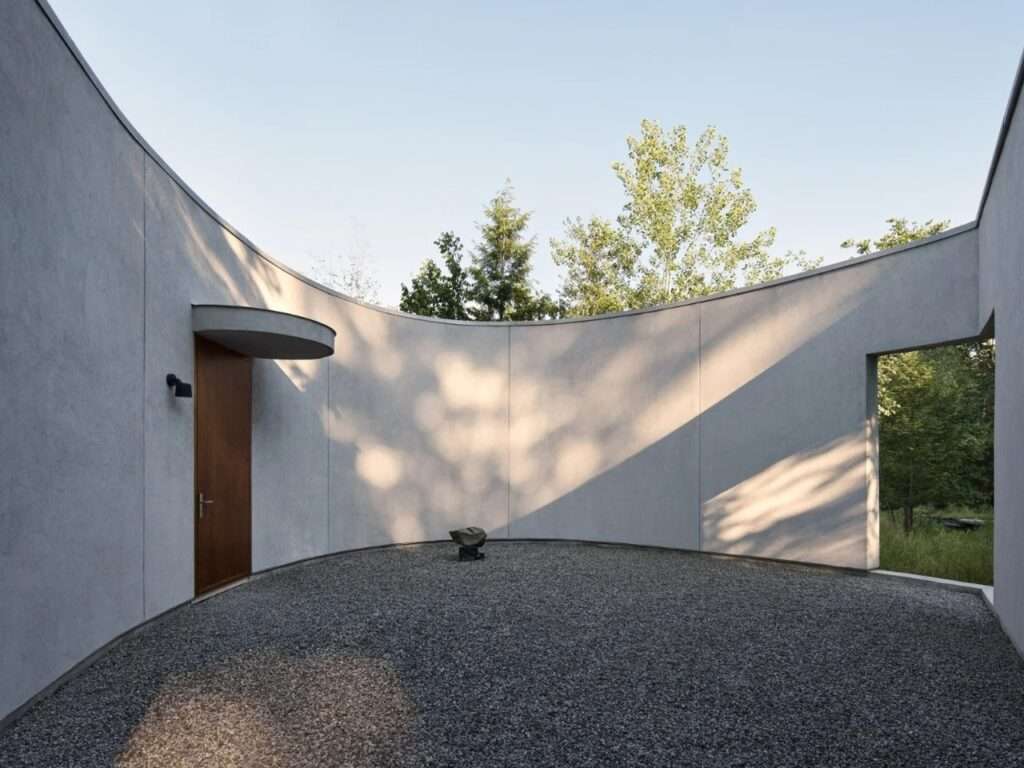 Curved inner courtyard of a modern pavilion with a gravel floor and harsh geometric shadows cast by sunlight.