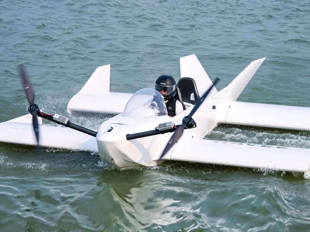 Front view of the Navee WaveFly 5X gliding fast through choppy water, with a pilot in a black helmet behind the transparent windshield amid splashing waves.