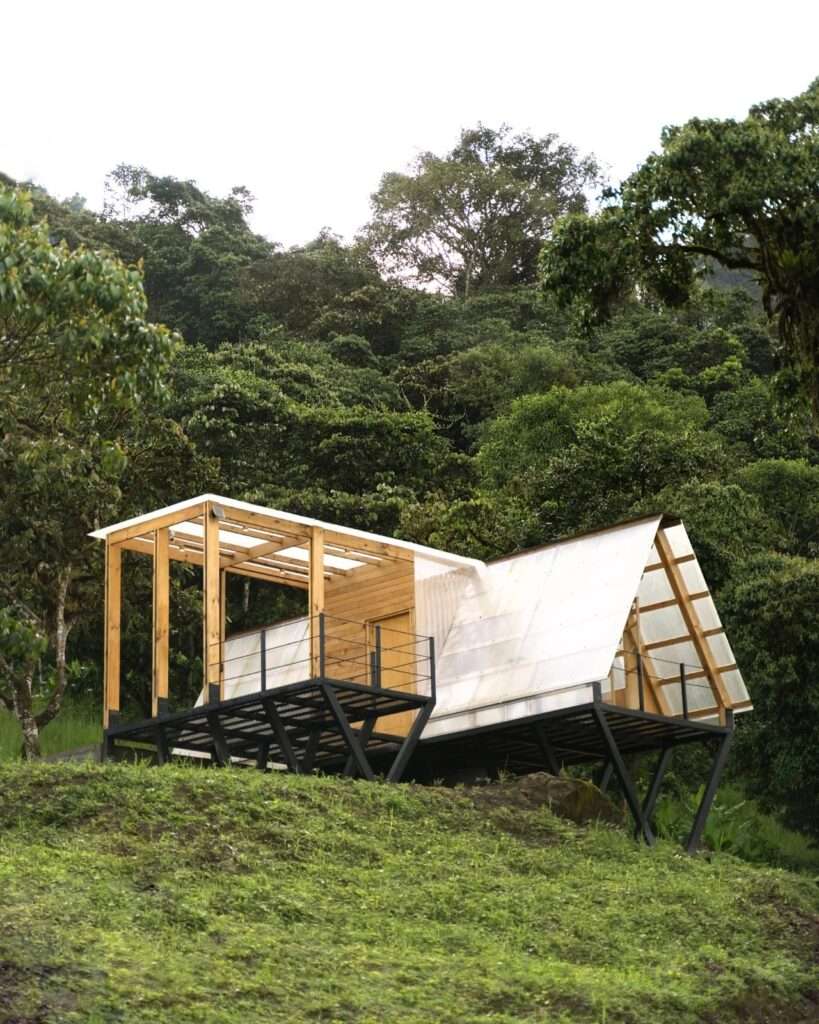 A compact wooden kitchen unit inside Casa 6-3 with a built-in stove and sink set beneath a triangular window framing the outdoor landscape.