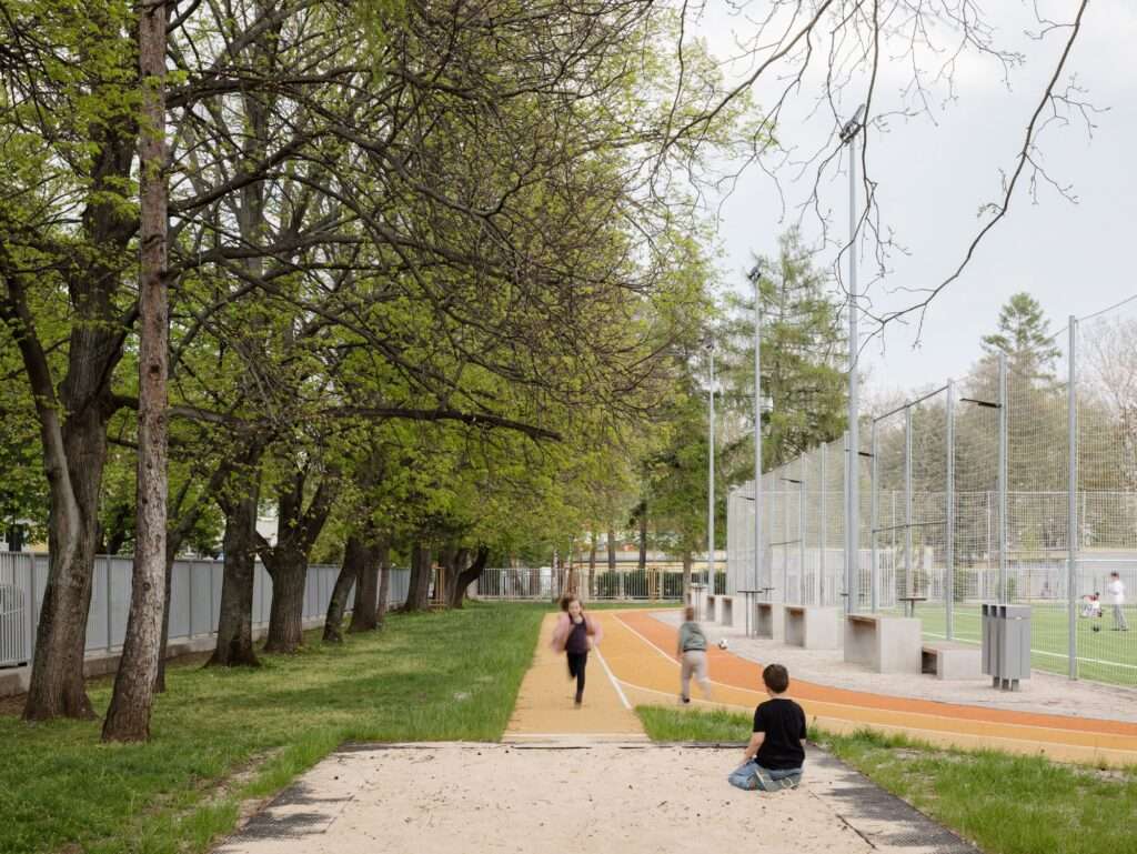 Children running on an orange running track with a long jump sand pit in the foreground at a renovated school sports facility.