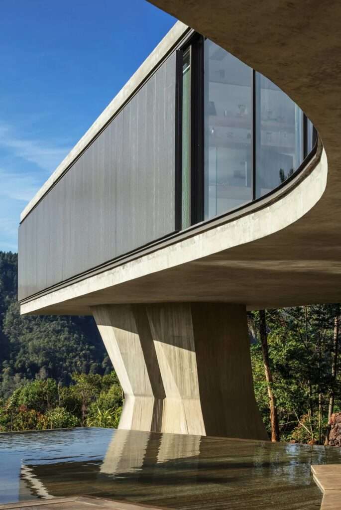 Xingu House elevated concrete volume supported by a thick, irregular concrete column overlooking a forested mountain valley.