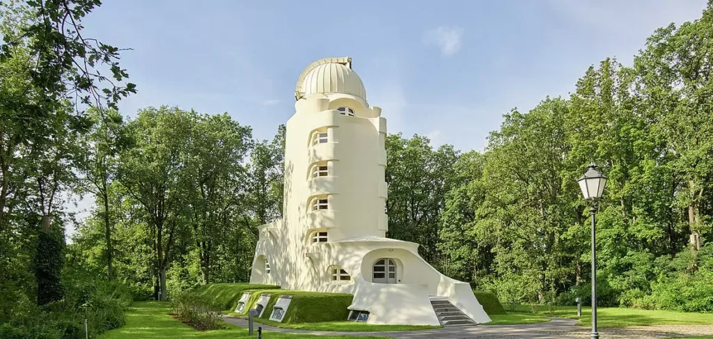 Wide panoramic landscape photograph of the iconic Einstein Tower surrounded by lush summer trees and manicured green lawns under a clear sky.