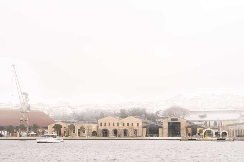 Distant waterfront panoramic view of the historic Beymen Tersane buildings on the Golden Horn under a foggy sky, with a crane on the left.